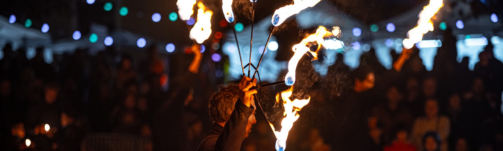 A fire juggler performs at a large outdoor nighttime event.