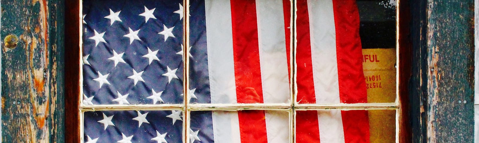 American flag behind a window in a distressed house.