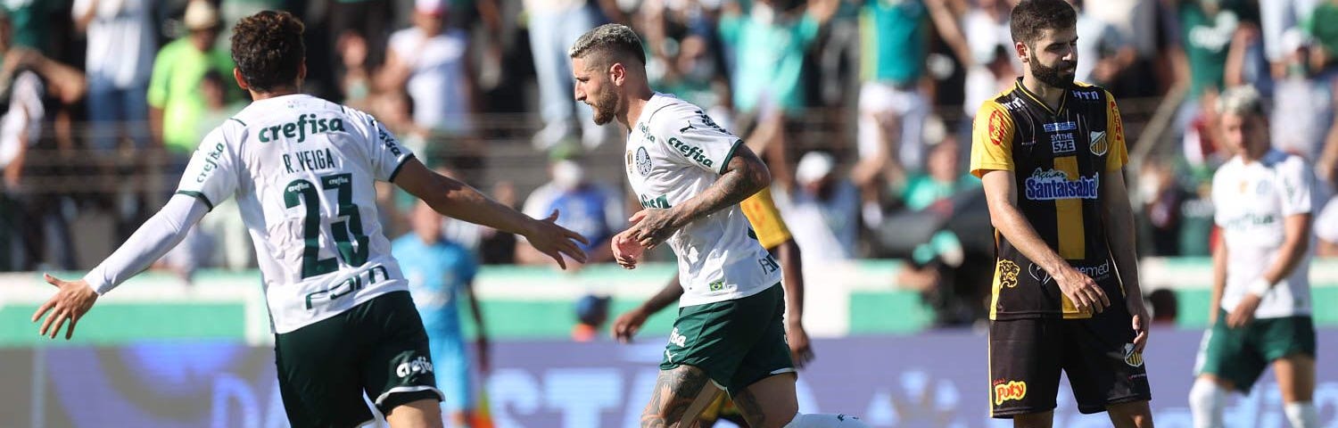 Zé Rafael comemora com Rafael Veiga o gol pelo Palmeiras contra o Novorizontno. Ele corre para a esquerda e está de lado, Veiga de costas com os braços abertos. Eles vestem camisa branca, calção verde e meias brancas.