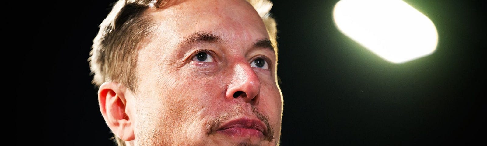 Elon Musk looking away, thinking.