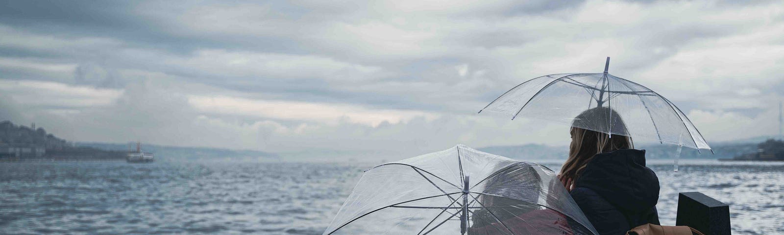 A photo of a mother and her child sitting on the dock beneath umbrellas in a storm.