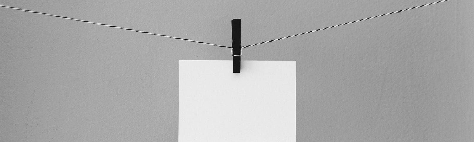 Sheet of blank white paper hanging by a black peg on a string against grey background