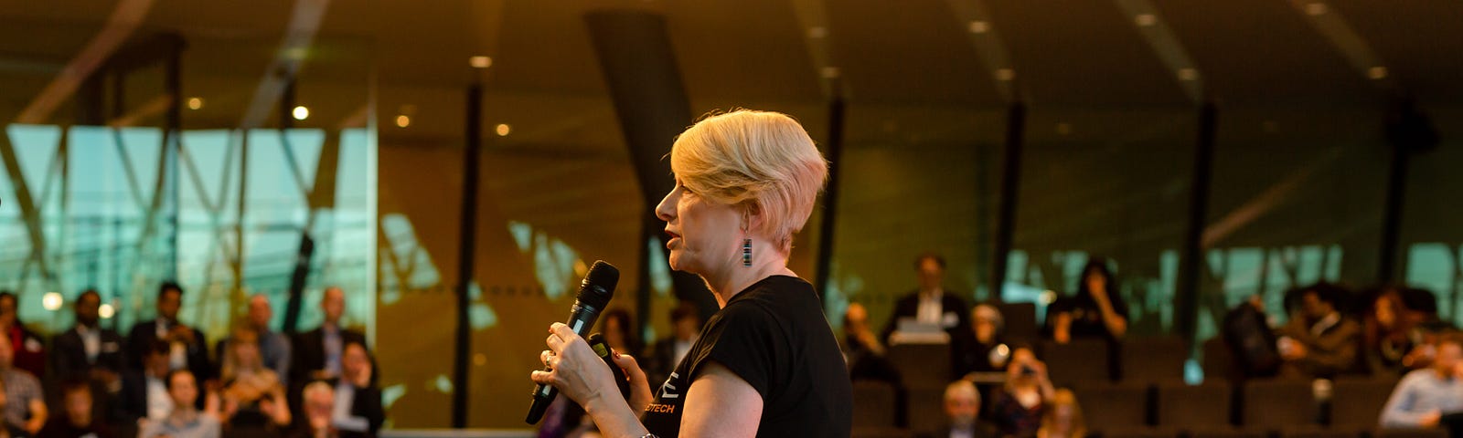 Professor Rose Luckin, Director of EDUCATE, stands with a microphone in front of a large audience at London’s City Hall
