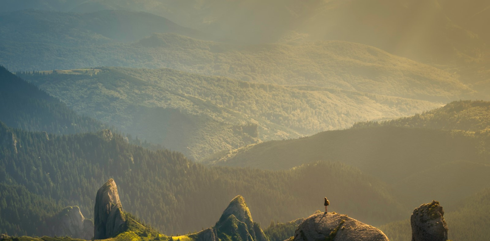 At dawn, a traveler stands at the top of a rock face, looking out over the valley below.