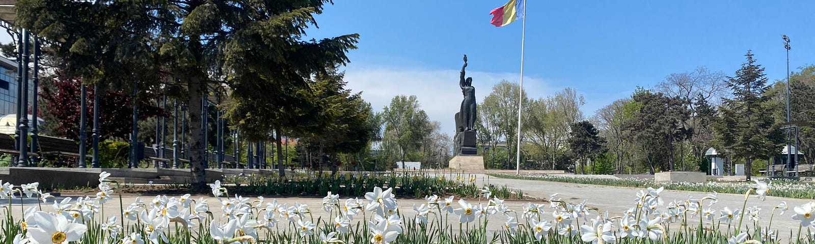 Park with flowers, statue and Romanian flag.