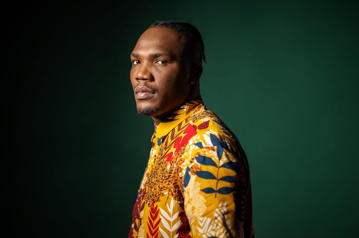 Handsome young Black man wearing colorful plant-inspired prints standing in profile while looking confidently at the camera.