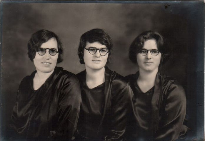 Black and white photograph of 3 young women wearing glasses and similar tops from the 1920s posing for a formal photograph.