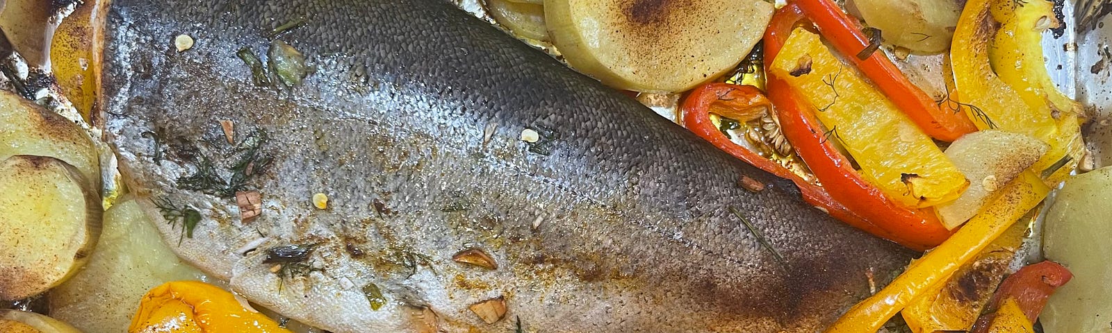 A grilled and baked whole trout with potatoes, vegetables, and herbs