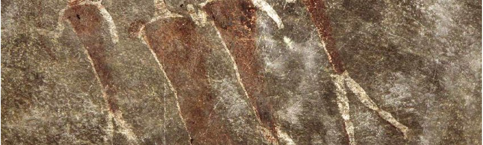 Stick figures in white of 4 creatures with heads like antelopes and body and feet like human, painted on brown rock surface.