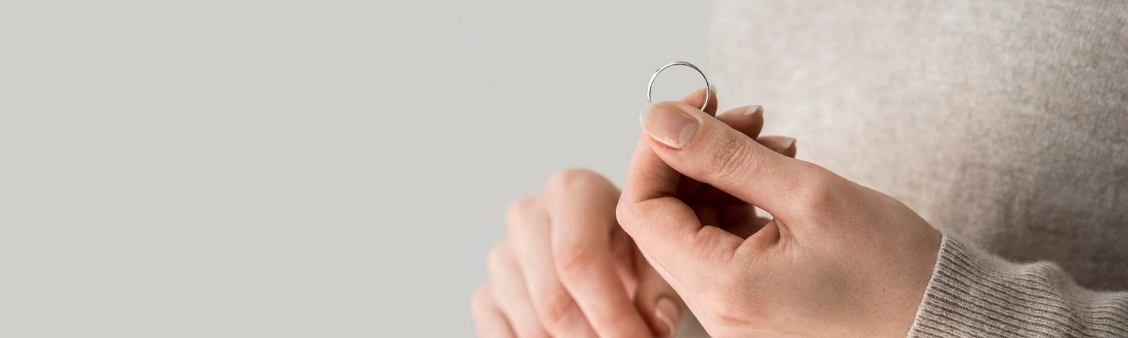 A female hand holding a gold wedding ring.