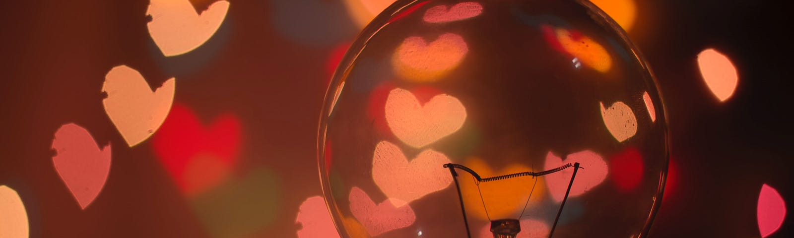 Close-up of a lightbulb with pale red lights in heart shapes surrounding it.