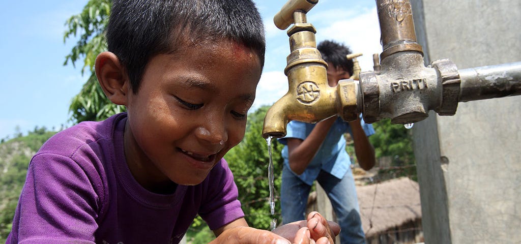 A little boy drinking from a water spigot.