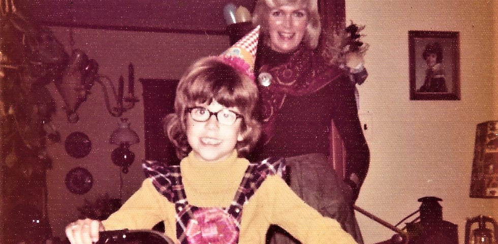 Author on her 8th birthday sitting on her new bike. Her mom in the background smiling.