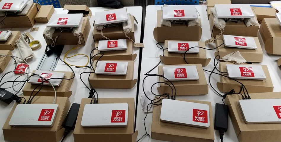 A set of WiFi routers and access points labeled with Mercy Corps stickers prepared for deployment