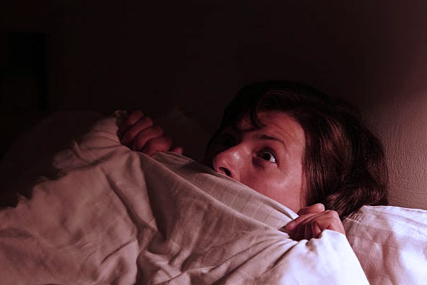 A girl is looking frightened and covering her body and half of her face with a blanket