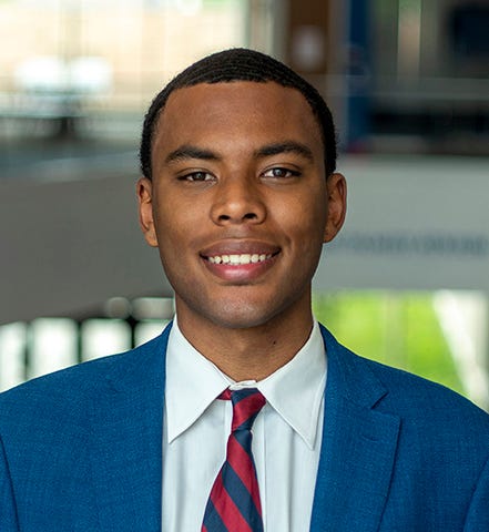 Malik Bauer photographed in Capitol Federal Hall wearing a blue suit jacket, white shirt and red-and-blue striped tie