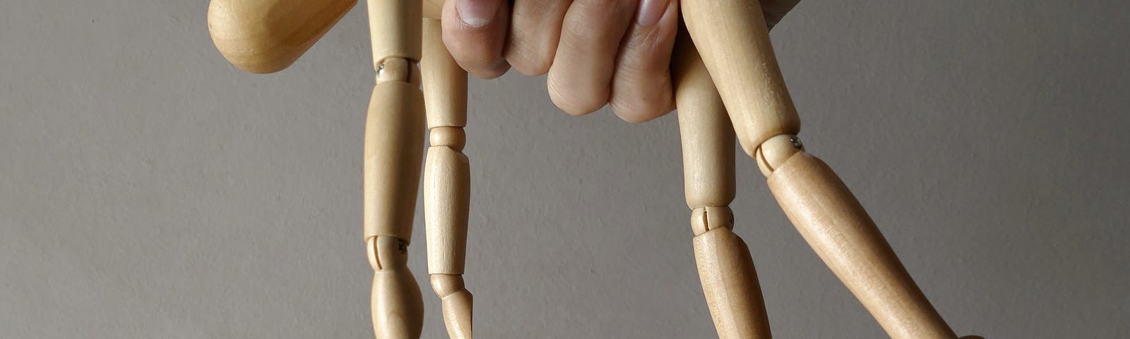 A figurine used by artists for drawing forms being gripped in a hand around the middle from above so their head, arms, and legs dangle.