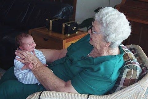 An aged great-grandmother holds and admires a new baby.