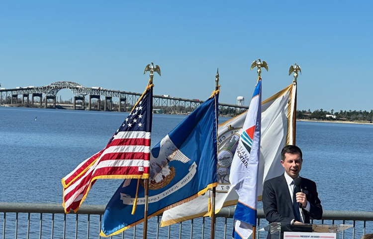 Secretary Buttigieg delivers remarks with the Calcasieu River Bridge in the background.