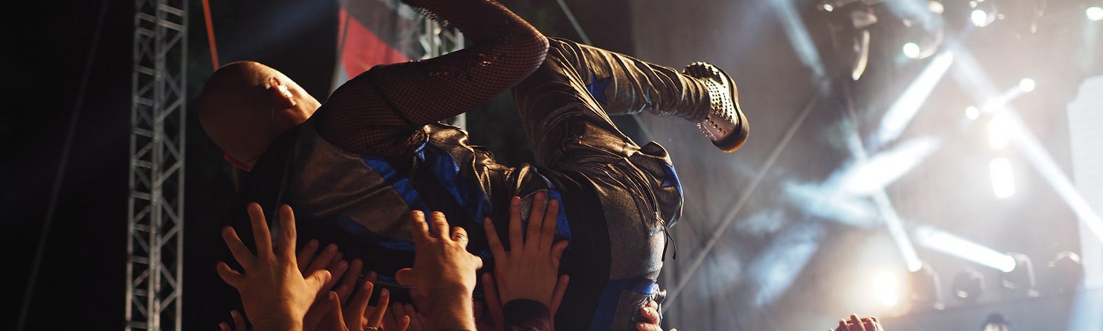 Person jumping, back first, into a crowd at a concert. Crowd surfing with lights in the background..