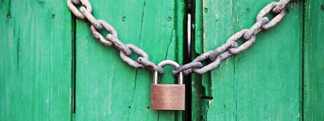 A green wooden door is secured by two silver metal chains that are held together by a closed padlock.
