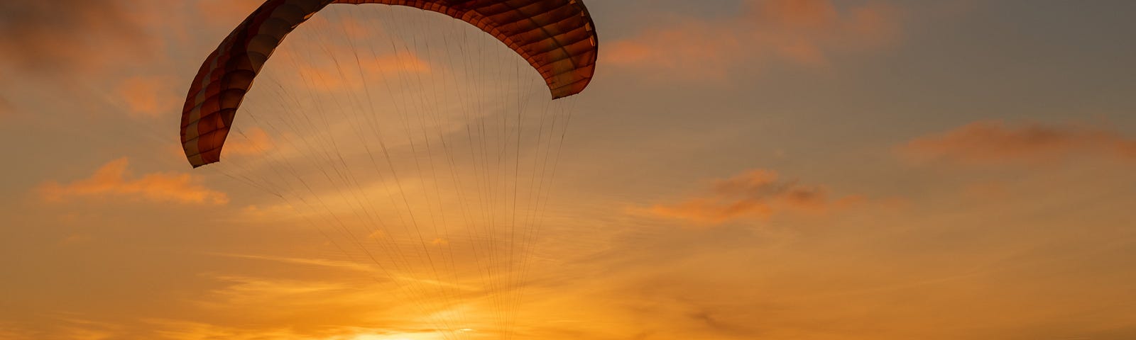 A man paragliding over a sea at sunset