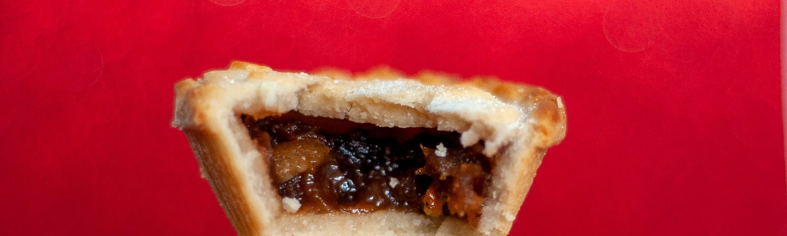 Three mince pies are stacked on top of each other, the top one has a bite taken out of it.