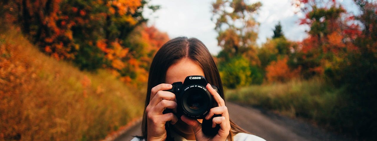 Woman holding up a camera in the woods.