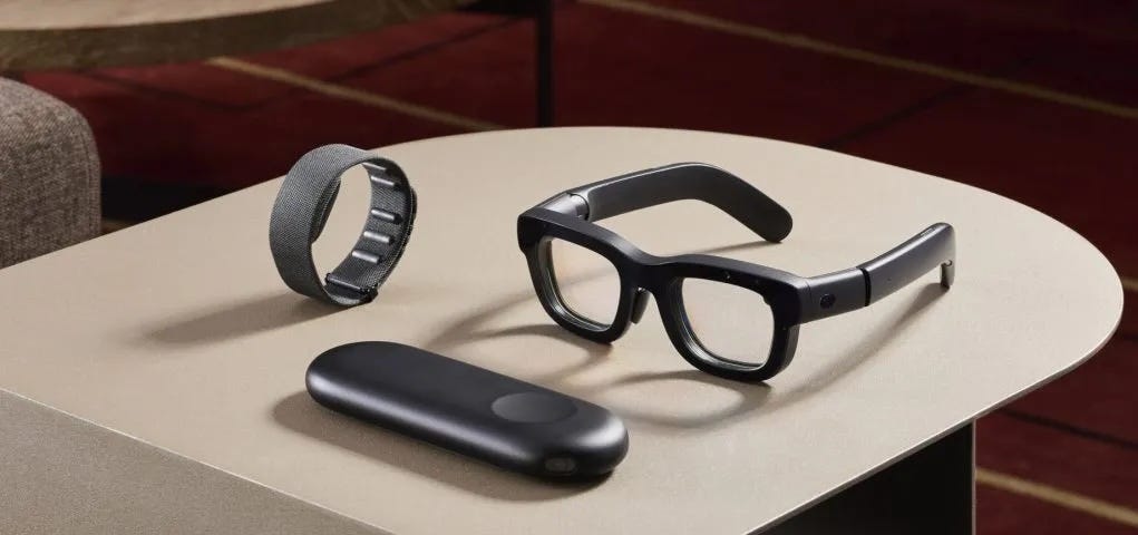 IMAGE: Meta Orion prototype, a pair of very thick Ray-ban glasses with a wristband and a puck approximately the size of a glasses pouch, all black