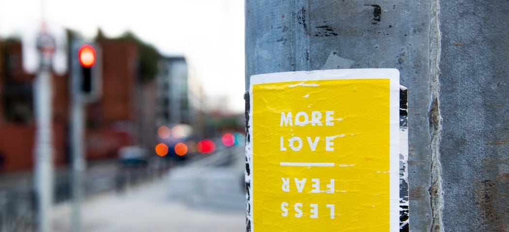 an image of a yellow poster that says “more love” “less fear” on a wall