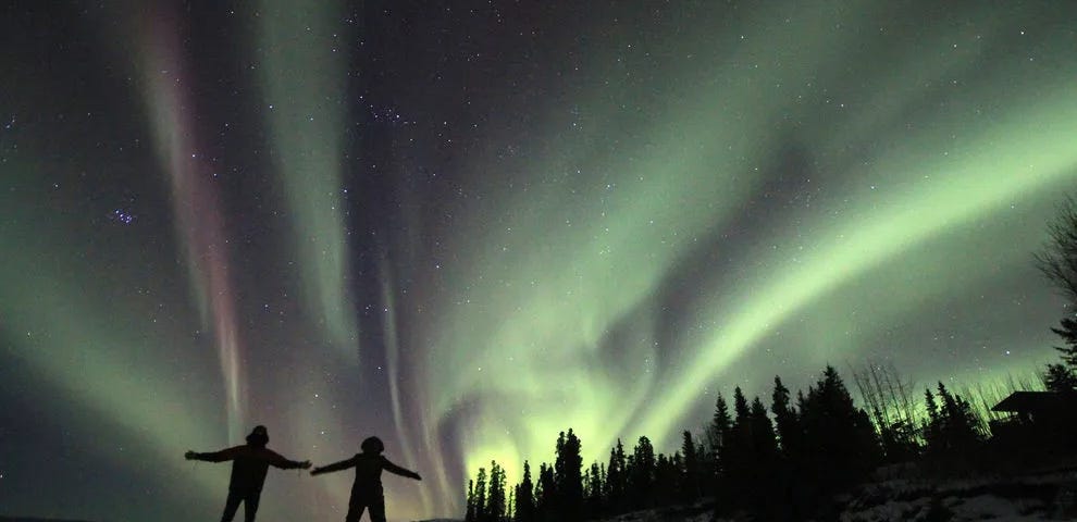 Two lucky travelers take in the northern lights while standing on a frozen lake in th Yukon region of Canada.