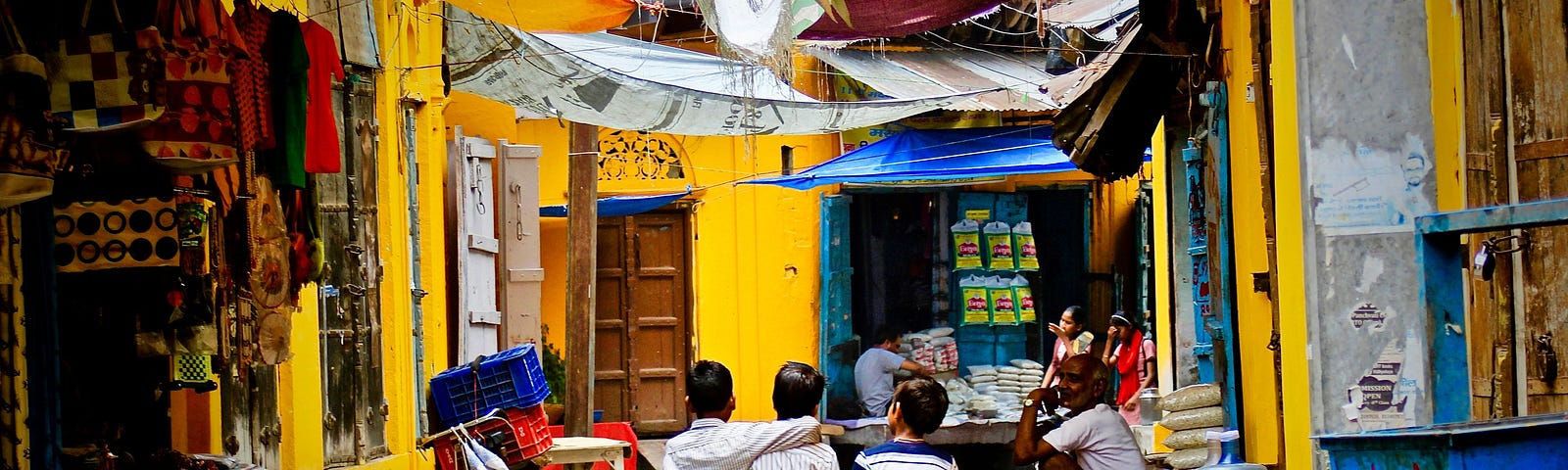 Three kids walking away from you down a street in India, arm in arm.