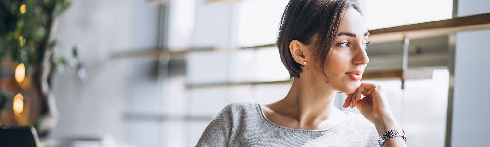 Woman sits in front of laptop looking out the window with a pensive expression