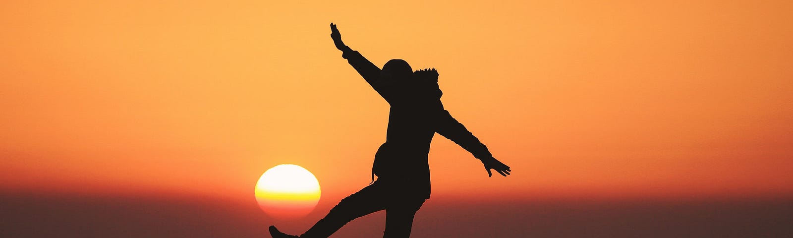 Silhouette of a person balancing on a rock in front of a sunset