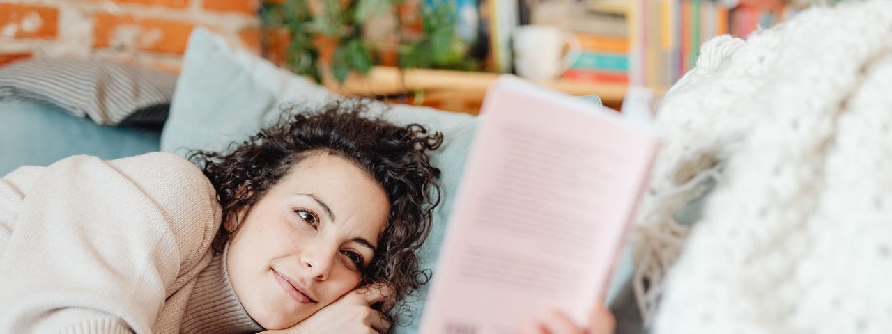 woman relaxing in bed & reading a book, with bookshelves in the background