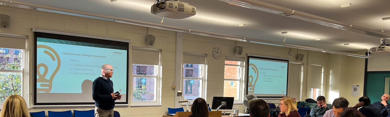 An image showing Professor Stuart Taberner addressing the first Horizons Institute collaborative lab. There are a number of people sat listening around groups of tables, and there is a powerpoint screen in the background.