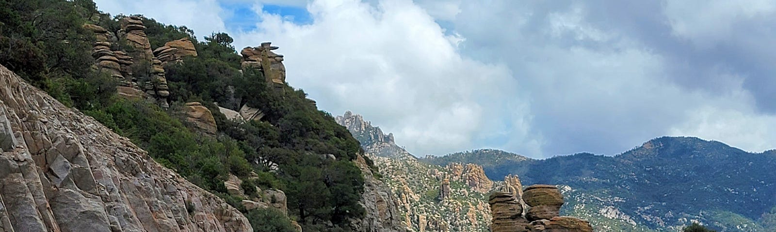 A winding highway going through hoodoo rock formations with green mountains and clouds in the background