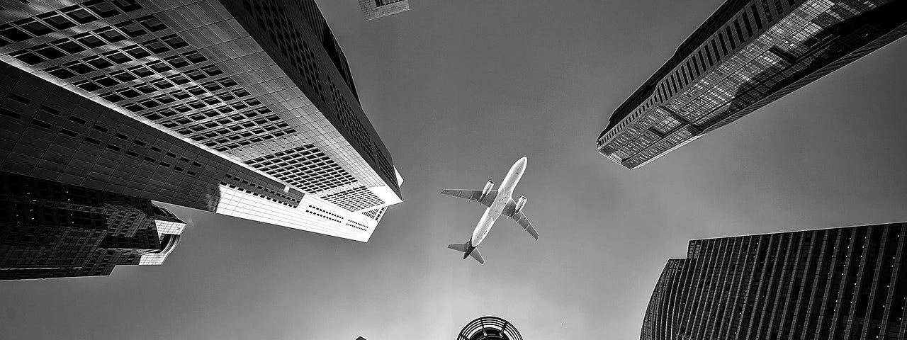 IMAGE: An airplane on flying on top of a few skyscrapers, seen from the ground