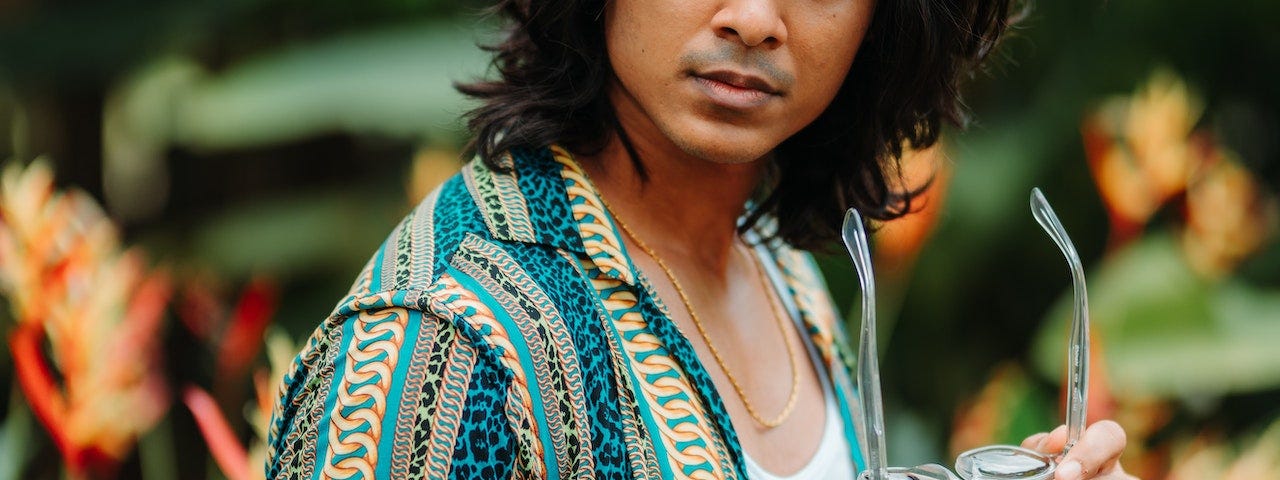 A beautiful man with long black hair looking over his shoulder.