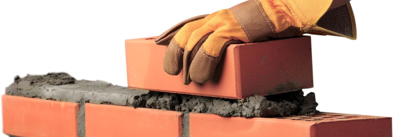 Gloved hand laying bricks.