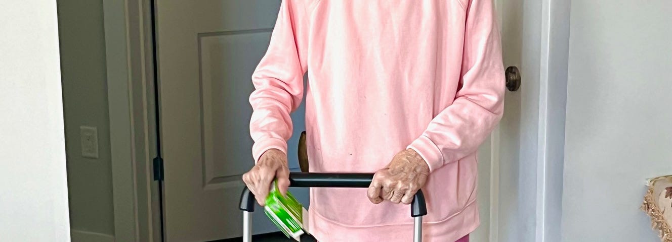 An elderly woman dressed in pink, with a pink headband, pushing a shopping cart