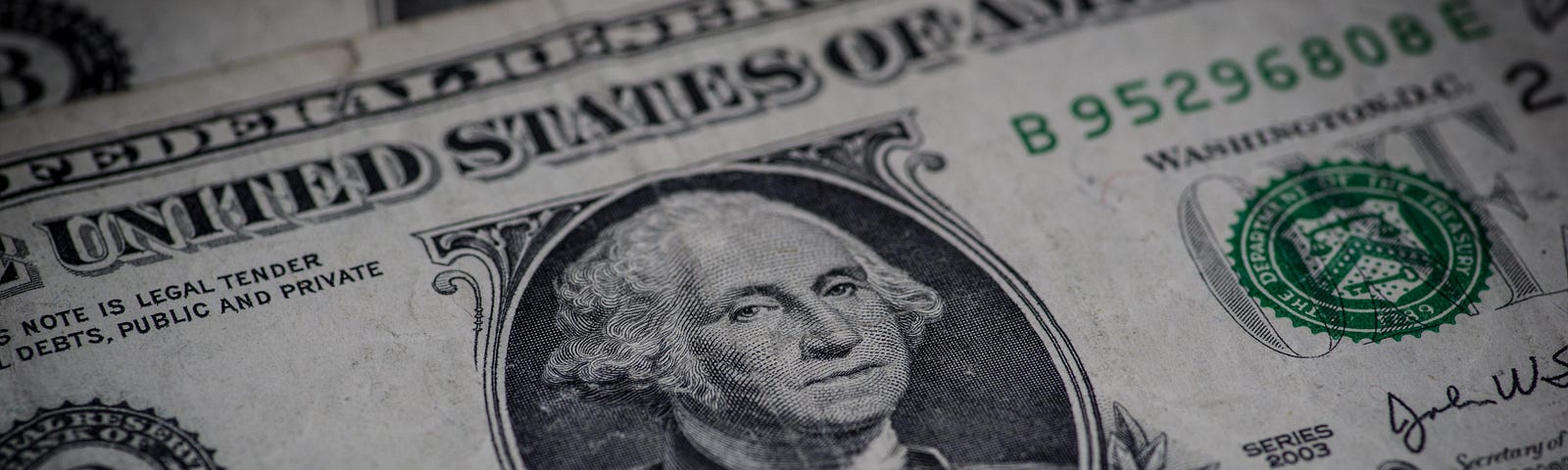 A United States one-dollar bill, worn from use, with two others beneath it in a small pile