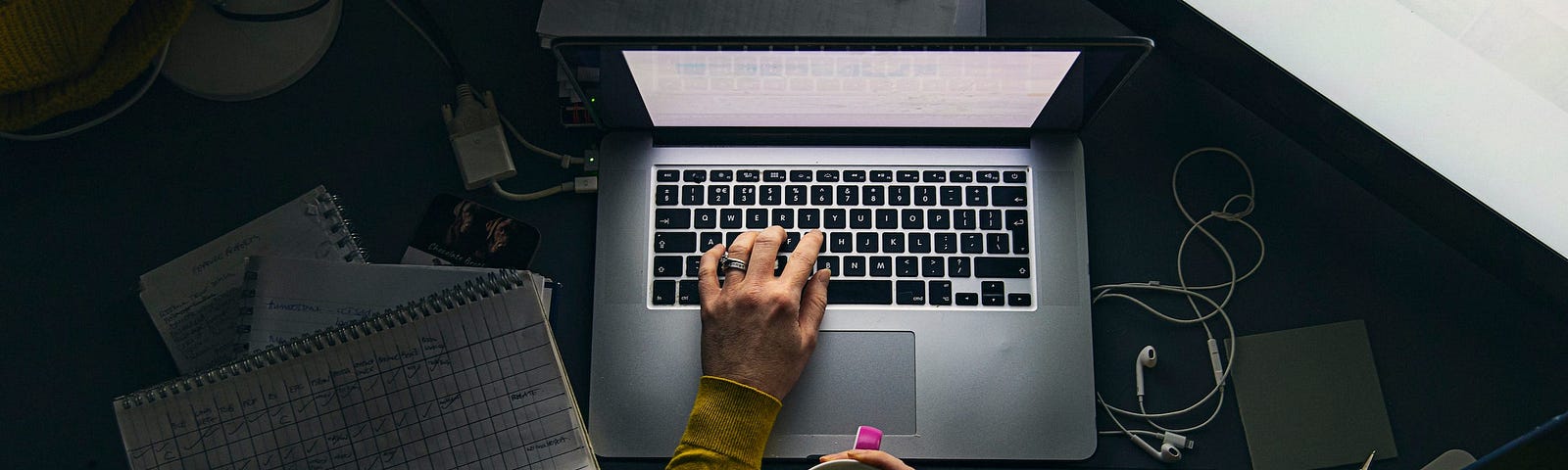 A person using their laptop at night and holding a cup of coffee.