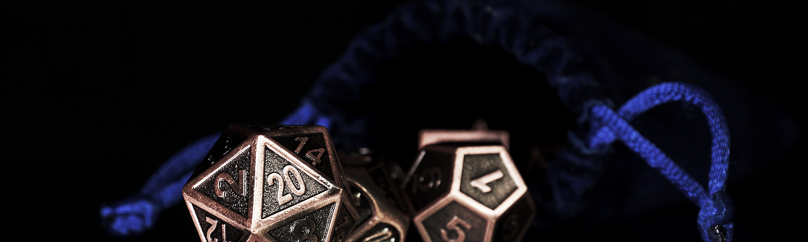 Image: Bronze D20 and D12 sitting in front of a blue velvet bag.