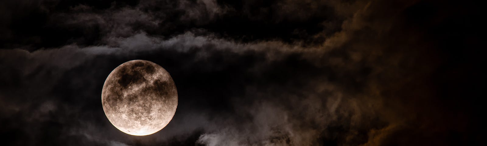 full moon in night sky behind clouds