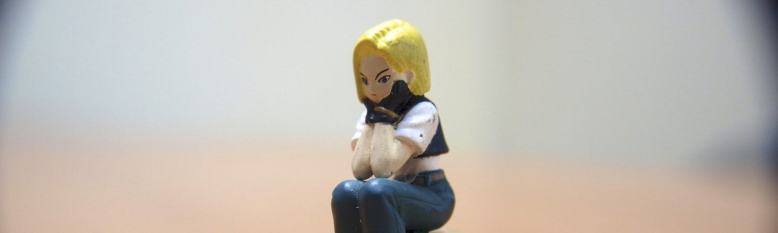 Figurine with blonde hair sits on a rock holding her head in her hands. The background is blurred.