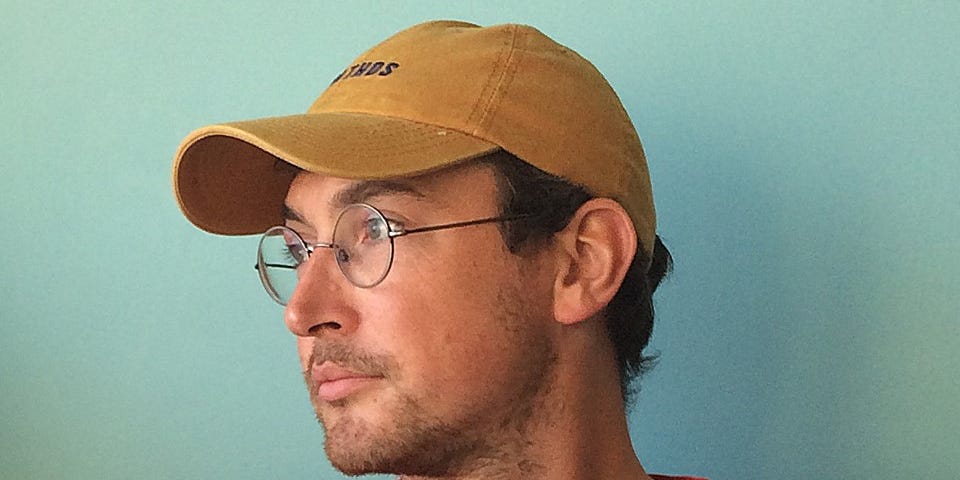 Photo of the illustrator Michael Kirkham wearing glasses and a baseball cap, looking to the left.
