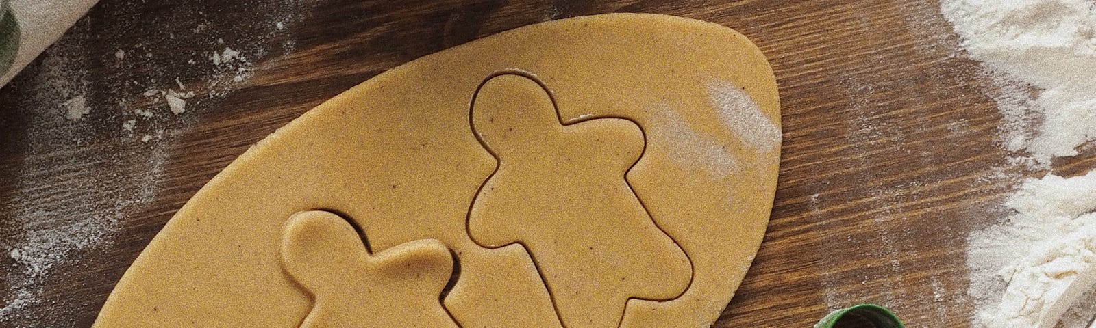 Gingerbread men being cut out of dough with cookie cutters