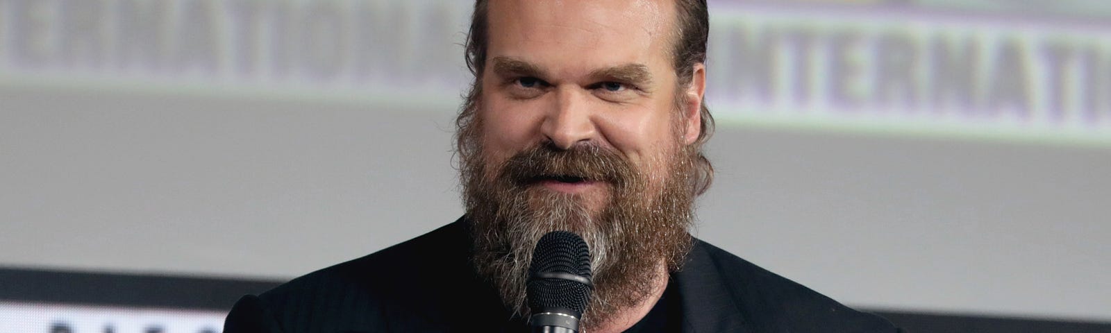 David Harbour holds a microphone.