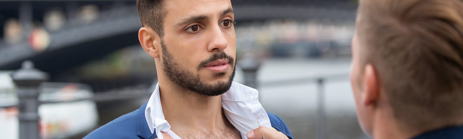 A man holding another man by the collar. Both look unhappy.